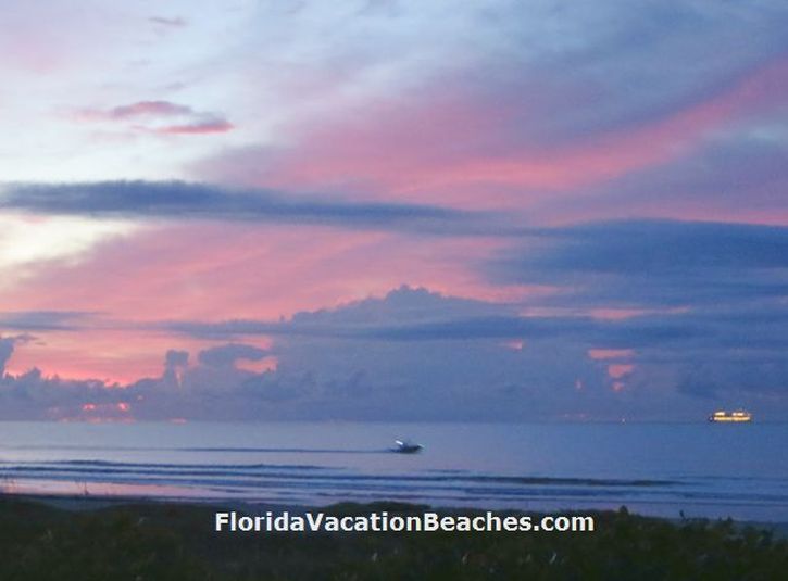 Colorful Cocoa Beach Florida Sunrise over Atlantic Ocean with clouds and Lights of a Cruise Ship + a small boat going by